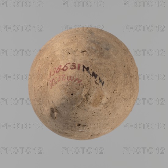 Vessel with hieratic inscription, Egyptian pottery conical vessel tapering toward the bottom, handcrafted clay vessel with upper part shoulders, neck, rim turned. Slightly irregular, widest approx. 3/4 of the height; narrow sloping shoulders; short wide neck; very gently rounded, widening rim; pointed bottom. Around half the height a trace of joining of two separately made parts. Surface leveled, outer probably covered with a layer of engobe. Made of Nile clay Vienna System. Remains of a hieratic inscription in black on the lower part of the belly. Rim damaged. Analogies cited; earlier dated to the 4th–5th Dynasty; Old Kingdom, Edfu. Dimensions: height 13.2 cm; diameter 5.8 cm rim; diameter 8.3 cm body., A rounded, dome-shaped object with a rough, pitted surface dominates the image, showing a tan to light brown color with small darker brown and gray speckles and blemishes; the background is a uniform light gray.