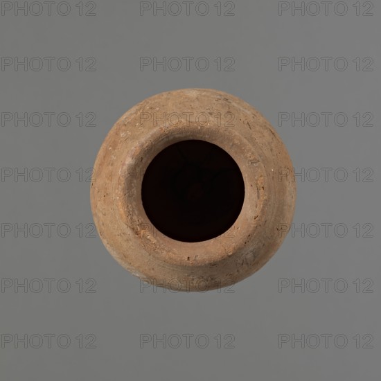 Vessel by, Egyptian pottery ceramic conical vessel tapering toward the bottom, irregular, widest approx. 3/4 of the height; narrow sloping shoulders; short wide neck; rounded outward rim slightly widening; pointed bottom. Handcrafted: upper part shoulders, neck, rim turned. Smooth surface; exterior probably coated by the potter with a layer of clay mixture applied by hand. Made of Nile clay NB2 Vienna System. Beige and red coloration. Vessel cracked along one wall; rim damaged. Analogies: parallels in Petrie Dendera, Abydos, Hope Akhmim, Reisner Mycerinus; Naga ed-Der, Brunton Qau and Badari, Mace Naga ed-Der II, Keiser et al. MDAIK 40, fig.9b. Old Kingdom, Edfu. Height 13 cm; rim diameter 6.3 cm; body diameter 9 cm., A round clay vessel viewed from above with a large dark opening in the center, the vessel surface showing a rough, textured appearance with small pits and imperfections; the clay is a warm brown color with lighter and darker brown variations, and the background is a flat ...