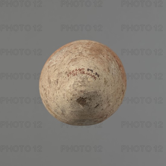 Vessel with hieratic inscription, Egyptian pottery, clay conical vessel tapering towards the bottom; irregular, widest approx. 3/4 of the height. Narrow, sloping shoulders; short, wide neck; very gently rounded, slightly flaring rim; pointed bottom. Handmade, upper part shoulders, neck, rim turned. Surface even, outer probably covered with engobe. Made of Nile clay NB2 Vienna System. Remains of a hieratic inscription in black on lower part of the belly. Quite well preserved—minor rim damage. Old Kingdom, ca. 2686–ca. 2181 BC; findspot Edfu. Dimensions: height 16.1 cm; rim diameter 6 cm; belly diameter 9 cm. Analogies: Petrie Dendera, Hope Akhmim, Reisner Mycerinus; Naga ed-Der III, Brunton Qau and Badari, Mace Naga ed-Der II, Petrie Abydos II, Keiser et al., MDAIK 40, fig. 9b., A roughly spherical object with a textured, weathered surface, showing areas of beige, light tan, brown, and hints of reddish-orange, suspended against a uniform gray background; the surface has irregular darker...