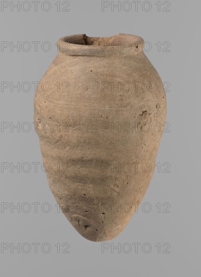 Vessel with hieratic inscription, Egyptian pottery ceramic conical vessel tapering toward the bottom with pointed base; narrow sloping shoulders, short wide neck, rounded slightly flaring rim. Handmade, upper part shoulders, neck, rim turned. Surface even, outer probably covered with engobe. Made of Nile clay NB2 Vienna System. Remains of a hieratic inscription in black faintly visible on lower belly. Very well preserved. Analogies cited in literature; earlier dated to the 4th–5th Dynasty; Old Kingdom, Edfu; height 14.9 cm, rim diameter 6.3 cm, body diameter 9.5 cm., A single rounded vessel with a narrow neck and flared rim sits against a plain background; the surface is textured and uneven with visible small pits and shallow scratches, showing an overall earthy brown color with subtle variations of lighter and darker brown tones and traces of pale gray; the rim appears slightly irregular and worn, and the body tapers to a rounded point with some rougher patches and small surface imper...