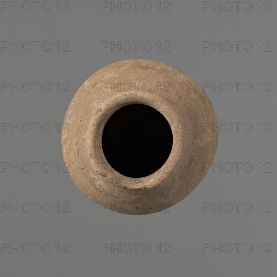 Vessel with hieratic inscription, Egyptian pottery ceramic, conical clay vessel tapering to a pointed bottom; narrow sloping shoulders, short wide neck, outward rounded rim slightly widening. Handcrafted with the upper part shoulders, neck, rim turned. Smooth exterior probably covered with engobe. Made of Nile clay NB2 Vienna System. Remains of a hieratic inscription in black on lower belly. Fairly well preserved with a damaged rim. Old Kingdom, ca. 2686–2181 BC earlier comparisons place similar forms in 4th–5th Dynasty. Height 14.9 cm; rim diameter 5.5 cm; belly diameter 8.9 cm. Analogies: Petrie Dendera, Abydos, Hope Akhmim, Reisner Mycerinus, Naga ed-Der, Brunton Qau and Badari, Mace Naga ed-Der II, Keiser, Avila, Dreyer, Jaritz, Laskowska-Kusztal MDAIK 40., A round, weathered clay vessel viewed from above with a wide, dark interior opening; the vessel surface shows a rough, uneven texture with small pits and scratches and displays shades of brown and tan, while the background is a ...