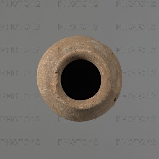 Vessel with hieratic inscription, Egyptian pottery, conical clay vessel tapering toward the bottom, irregular, widest at approximately 3/4 of the height. Narrow, sloping shoulders; short, wide neck; gently rounded, slightly flaring rim; pointed bottom. Handcrafted; upper part shoulders, neck, rim turned. Smooth surface, externally probably covered with a layer of engobe. Made of Nile clay NB2 Vienna System. Remains of a hieratic inscription in black on the lower part of the belly. Fairly well preserved; damage to the rim. Old Kingdom, Edfu. Height 14.6 cm; rim diameter 5.8 cm; belly diameter 8.7 cm. Analogies/citations: Petrie, Dendera; Hope, Akhmim; Reisner, Mycerinus; Brunton, Qau and Badari; Mace, Naga ed-Der II; Reisner, Naga ed-Der III; Petrie, Abydos II; Keiser et al., MDAIK 40; dated ca. 2686–2181 BC., A round, weathered clay vessel viewed from above with a wide circular opening showing a deep black interior, the exterior surface textured and pitted with an earthy brown color an...