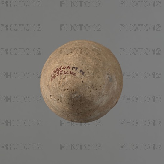 Vessel with hieratic inscription. Conical clay vessel tapering toward the bottom with narrow, sloping shoulders, short wide neck, gently rounded slightly flaring rim, and pointed bottom. Handcrafted: upper part shoulders, neck, rim turned. Smooth surface, externally probably covered with engobe. Made of Nile clay NB2 Vienna System. Remains of a hieratic inscription in black on the lower part of the belly. Fairly well preserved; rim damaged. Old Kingdom, ca. 2686–2181 BC. Height 14.6 cm; rim diameter 5.8 cm; belly diameter 8.7 cm. Analogies: Petrie, Dendera pl. XVI.2; Hope, Akhmim fig.7 type AIVa 2bi; Reisner, Mycerinus p.212 fig.64; Brunton, Qau and Badari pl. LXXXI type 77N; Mace, Naga ed-Der II figs.87.11–14,16–25; Reisner, Naga ed-Der III figs.28–33; Petrie, Abydos II pl. XLIII 79–80; Keiser, Avila, Dreyer, Jaritz, Laskowska-Kusztal, MDAIK 40 fig.9b., A round, weathered object with a rough, pitted surface in shades of brown and tan floats against a flat gray background; the object s...