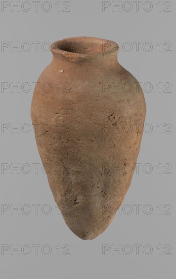 Vessel with hieratic inscription; ceramics, Egyptian clay Nile clay NB2, Vienna System. Conical vessel tapering towards the bottom, irregular, widest approx. 3/4 of the height. Narrow, slightly sloping shoulders; short, wide neck; very gently rounded, slightly flaring rim; pointed bottom. Handcrafted; upper part shoulders, neck, rim turned. Surface leveled. Remains of a hieratic inscription in black on lower part of the belly. Quite well preserved with slight damage to the rim. Old Kingdom, ca. 2686–2181 BC. Height 15.2 cm; rim diameter 5.1 cm; belly diameter 8.3 cm. Comparable typologies: Petrie Dendera, Abydos, Hope Akhmim, Reisner Mycerinus, Naga ed-Der, Brunton Qau and Badari, Mace Naga ed-Der II, Keiser et al., A single, tall clay vessel with a rounded shoulder and a narrowed neck tapering to a small flared rim is shown against a plain gray background; the vessel surface is rough and pitted with visible texture and small indentations, and its color is mostly earthy brown with patc...