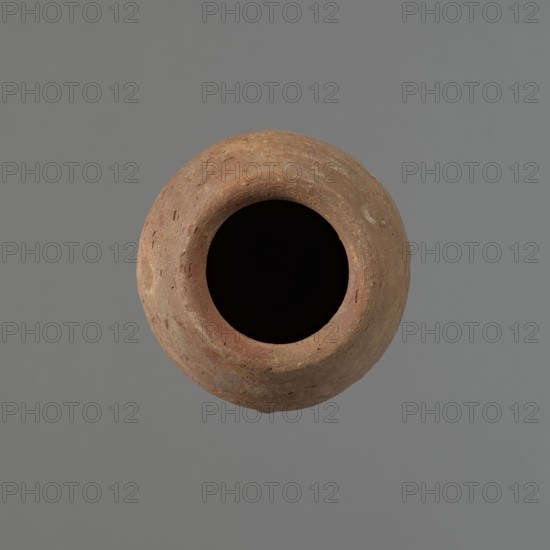 Vessel with hieratic inscription, Egyptian pottery ceramic conical vessel tapering toward the bottom, irregular, widest at approx. 3/4 of the height; narrow, sloping shoulders; short, wide neck; very gently rounded rim slightly widening; pointed bottom. Handmade, upper part shoulders, neck, rim turned. Surface even, outer probably covered with a layer of engobe. Made of Nile clay NB2 Vienna System. Remains of a hieratic inscription in black on lower part of the belly. Well preserved. Analogies cited; earlier dated to the Old Kingdom ca. 2686–ca. 2181 BC. Find from Edfu. Dimensions: height 14.9 cm; rim diameter 5.7 cm; belly diameter 8 cm., A round earthenware vessel seen from above with a wide dark opening at its center, the body showing a rough textured surface in shades of brown and reddish-brown with small pits and uneven patches, set against a solid gray background.
