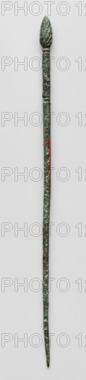 Hairpin with a head in the form of a pine cone; maker, attributed to Semerau-Siemianowski, Wladyslaw 1849–1938 note: possible cataloger; pine cone motif; women's accessory; 5th–4th century BC; Etruria; decoration; weight 6 g; height 14.2 cm; diameter 0.4 cm, A long slender object with a textured, slightly twisted top resembling a bud or flame, attached to a narrow shaft that tapers to a pointed end; the surface shows a rough, corroded texture with patches of greenish patina, darker brown and black areas, and small spots of red; the background is a light neutral color.