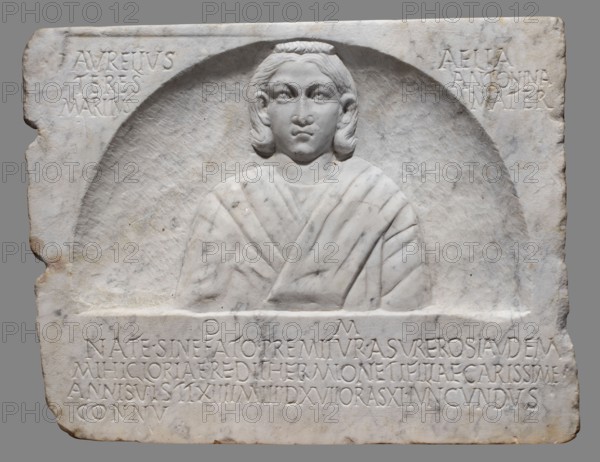 Funerary stele with a depiction of the deceased Hermiones and a Latin inscription, unknown Roman workshop, female images, sepulchral funerary architecture, Latin inscriptions, 240–245, Roman Empire 27 BC–476, slab, height 47.5 cm, width 60.5 cm, depth 6 cm, weight 32 kg, A carved stone relief depicting a bust of a person set within a shallow arched niche, the figure shown from the chest up with stylized hair and a draped garment, all carved in pale white marble with subtle gray veining and slight brownish discoloration in places; the rectangular surrounding stone has a rougher texture with chips and worn edges, and there are several areas of shadowed carving creating depth around the niche and garment folds.