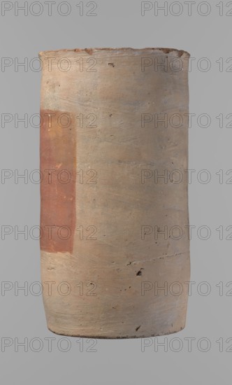 Canopic urn, clay, cylindrical shape with flat bottom and flat straight rim. Made on the wheel from Nile clay type NB2, Vienna System. Bottom trimmed with a knife; surface leveled. Outer wall painted with a red rectangle 11.5 cm wide × 11 cm high. Light brown color. Rim partially filled with plaster and painted preservation quite good. New Kingdom, ca. 1550–1069 BC, Deir el-Medina. Vessel; height 23.5 cm, rim diameter 12.5 cm, bottom diameter 11.4 cm., canopic urn function., A cylindrical earthenware vessel with a matte, slightly rough surface in shades of beige and tan, showing a rectangular patch of reddish-brown on one side; the vessel displays small dark specks and pits, horizontal striations and subtle tonal variations in grayish-beige, with a slightly uneven rim and a darker beige base against a neutral gray background.
