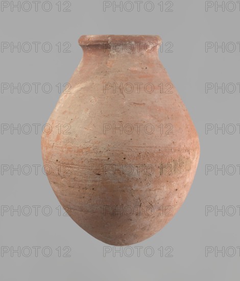 Vessel with an ovoid belly, a wide short neck and a rounded bottom. Straight, upturned rim. Wheel-made from Nile clay of type NB2 Vienna System. Surface levelled and outer surface covered with engobe. Outer surface red, inner surface yellowish-brown. Firing hole at the widest circumference approx. 1 cm diameter. Well-preserved. ca. 1550–1295 BC; New Kingdom, 18th Dynasty. From Deir el-Medina. Vessel; height 27 cm, rim diameter 11 cm, body diameter 20.5 cm., A large rounded clay vessel with a narrow flared neck and a slightly flattened rim, showing a rough, textured surface with visible tool marks and small pits; the vessel displays a range of earthy colors including terracotta, pale orange, light brown, and spots of beige, with subtle variations and patches of lighter and darker tones across its curved body, set against a smooth neutral gray background.