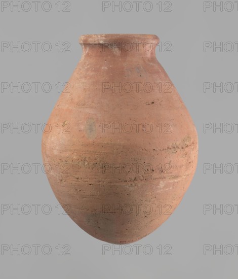 Vessel with an ovoid belly, a wide short neck and a rounded bottom. Straight, upturned rim. Wheel-made from Nile clay of type NB2 Vienna System. Surface levelled; outer surface covered with engobe. Outer surface red, inner surface yellowish-brown. Firing hole at the widest circumference of the body, approx. 1 cm diameter. Well-preserved; approx. 1550–1295 BC, New Kingdom, 18th Dynasty, Deir el-Medina. Vessel; height 27 cm, rim diameter 11 cm, body diameter 20.5 cm., A rounded terracotta vessel with a narrow neck and flared rim, showing a weathered, matte surface with visible texture and small pits; the jar is predominantly warm reddish-brown with areas of paler pinkish-brown and muted tan, plus a few faint grayish smudges and darker brown spots; the form is bulbous toward the lower half and tapers toward the top, and the rim edge appears slightly irregular and worn.