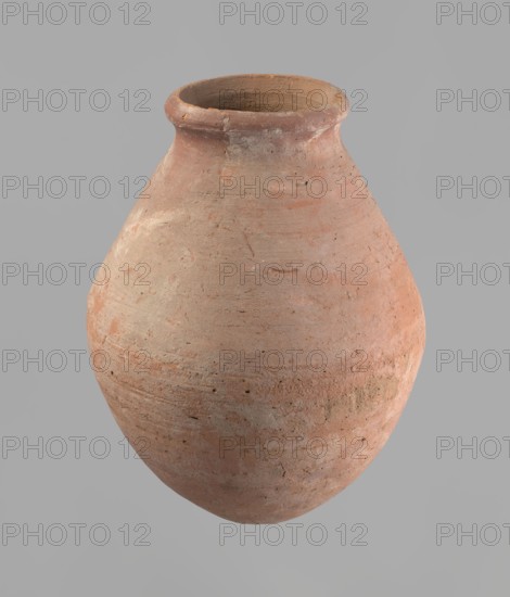 Vessel with an ovoid belly, a wide short neck and a rounded bottom. Straight, upturned rim. Wheel-made from Nile clay of type NB2 Vienna System. Surface levelled and outer surface covered with engobe. Outer surface red; inner surface yellowish-brown. Firing hole at the widest circumference, approx. 1 cm diameter. Well-preserved; approx. 1550–1295 BC, New Kingdom, 18th Dynasty, from Deir el-Medina. Vessel; height 27 cm, rim diameter 11 cm, body diameter 20.5 cm., A rounded clay vessel with a narrow neck and slightly flared rim occupies the image, showing a rough, textured surface with visible tool marks and small pits; the vessel displays a mix of earthy colors including terracotta, beige, pale orange, and hints of gray, with subtle variations and darker spots across its curved body, set against a uniform light gray background.