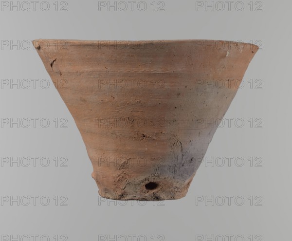 Bowl. Vessel flower pot with a conical shape and a flat bottom. Irregular walls. Straight, flat, slightly flaring, asymmetrical rim. Vessel made on the wheel of Nile clay type NB2 according to the Vienna System classification. Irregular bottom, cut off with a string. There is a 3.2 cm diameter hole in the bottom. In the lower part of the vessel, right next to the bottom, there are clear indentations that are the potter's fingerprints. The surface of the vessel is smooth. The colour of the vessel is reddish-brown. The condition is good, with only minor damage to the clay on the rim. ca. 1550–ca. 1069 BC; New Kingdom, Deir el-Medina. Vessel. Height 18 cm; diameter 15.8 cm rim; diameter 9.5 cm bottom., A large, weathered clay pot with a flared rim fills the frame, showing a surface texture of concentric wheel marks, rough patches, and small pits; the pot displays earthy tones of reddish-brown, terracotta, and areas of grayish-brown, with darker smudges and lighter flecks on the body; the ...