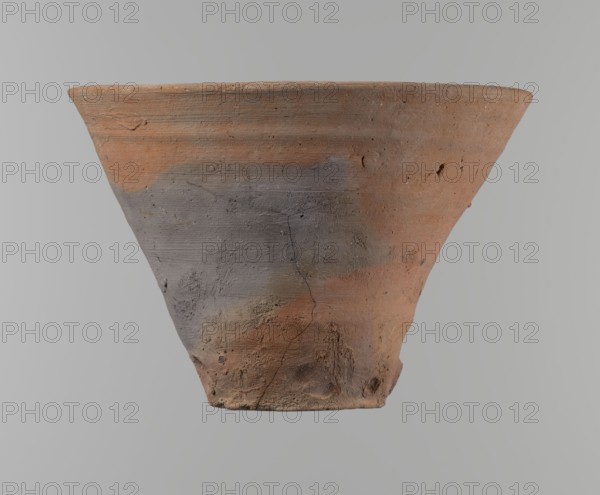 Bowl. Vessel flower pot with a conical shape and a flat bottom. Irregular walls. Straight, flat, slightly flaring, asymmetrical rim. Made on the wheel of Nile clay type NB2 Vienna System. Irregular bottom, cut off with a string; 3.2 cm diameter hole in the bottom. Potter's fingerprints as clear indentations in the lower part next to the bottom. Smooth surface. Reddish-brown color. Condition good, with only minor damage to the clay on the rim. ca. 1550–ca. 1069 BC; New Kingdom, Deir el-Medina. Vessel; height 18 cm, diameter 15.8 cm rim, diameter 9.5 cm bottom., A conical clay pot viewed from the side with a wide rim tapering to a narrower base, showing a rough, textured surface with visible cracks and small pits; the pot displays a mix of reddish-brown and gray areas, with some darker and lighter patches, and a matte, weathered finish against a neutral gray background.