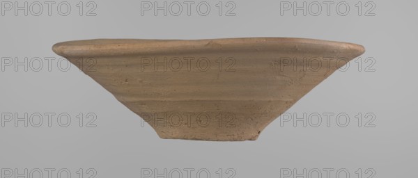 Bowl, Bowl with a conical shape and a flat bottom, slightly asymmetrical. Straight, flaring rim. Vessel made on the wheel of Nile clay type NB2 Vienna System. The bottom is cut off with a knife. Surface leveled. The outer part of the vessel is finished to approximately half its height with a knife or similar tool. Color of the vessel: yellow-red. Vessel reconstructed from two original fragments. c. 1550–c. 1069 BC, New Kingdom Ramesside period?, from Deir el-Medina. Ceramic bowl; height 9.2 cm; rim diameter 27.8 cm; bottom diameter 8.4 cm., A shallow, wide bowl viewed from the side with a flared rim and a tapered base, made of an unglazed clay material showing a textured, slightly rough surface; the object is predominantly light brown with variations of tan and beige, and the background is a smooth light gray.