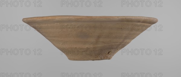 Bowl, Bowl with a conical shape and a flat bottom, slightly asymmetrical. Straight, flaring rim. Vessel made on the wheel of Nile clay type NB2 according to the Vienna System classification. The bottom is cut off with a knife. Surface leveled. The outer part of the vessel is finished to approximately half its height with a knife or similar tool. Color of the vessel: yellow-red. Vessel reconstructed from two original fragments. c. 1550–c. 1069 BC; New Kingdom Ramesside period?, Deir el-Medina. Vessel; height 9.2 cm, diameter 27.8 cm rim, diameter 8.4 cm bottom., An object resembling a shallow, wide bowl or dish is centered against a plain gray background; its surface shows a rough, textured finish with irregularities and small pits, and the visible colors include shades of brown, tan, and subtle hints of darker brown, with the background appearing light gray.