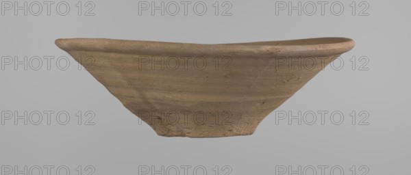 Bowl, Bowl with a conical shape and a flat bottom, slightly asymmetrical. Straight, flaring rim. Vessel made on the wheel of Nile clay type NB2 Vienna System. The bottom is cut off with a knife. Surface leveled. The outer part of the vessel is finished to approximately half its height with a knife or similar tool. Color of the vessel: yellow-red. Vessel reconstructed from two original fragments. c. 1550–c. 1069 BC; New Kingdom Ramesside period?. From Deir el-Medina. Ceramic bowl; height 9.2 cm, rim diameter 27.8 cm, bottom diameter 8.4 cm., A shallow, wide bowl-shaped object made of a coarse, clay-like material in shades of tan and light brown, shown from the side against a plain light gray background; the rim is slightly uneven and rounded, the surface displays horizontal wheel-like ridges and subtle texture variations with small rough patches and specks, and the base tapers inward to a narrower, rougher foot.