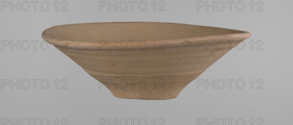 Bowl, Bowl with a conical shape and a flat bottom, slightly asymmetrical; straight, flaring rim. Vessel made on the wheel of Nile clay type NB2 Vienna System. Bottom cut off with a knife; surface leveled. Outer part finished to approximately half its height with a knife or similar tool. Color yellow-red. Vessel reconstructed from two original fragments. c. 1550–c. 1069 BC, New Kingdom Ramesside period?, from Deir el-Medina. Ceramic clay vessel; height 9.2 cm, rim diameter 27.8 cm, bottom diameter 8.4 cm., A shallow, wide bowl-shaped ceramic object with a rough, unglazed surface in shades of tan and light brown, showing concentric horizontal ridges and subtle speckling; the rim is slightly thicker and rounded, while the base tapers inward to a narrower foot; the background is a smooth, uniform light gray.