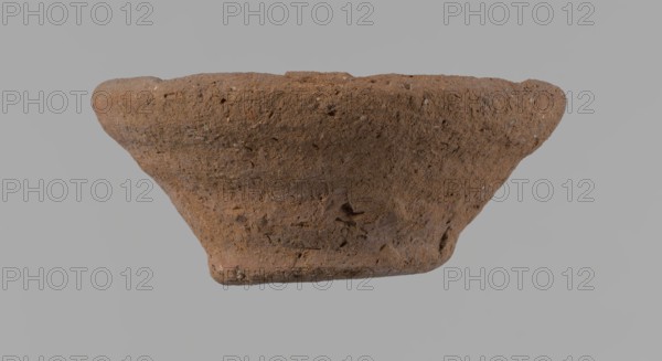 Bowl, probably votive, conical shape with a flat bottom. Irregular walls; straight rim slightly flaring; irregular bottom, probably cut off with a string. Wheel-made vessel of Nile clay type NC Vienna System classification. Surface only slightly leveled. Vessel color: brown. Well-preserved with only minor surface erosion. c. 1550–c. 1069 BC New Kingdom, Deir el-Medina. Vessel; height 3.7 cm, diameter 8.2 cm lip, diameter 4.2 cm bottom., A rough-textured, bowl-shaped object with an uneven rim and a tapered base, shown against a plain neutral background, displaying a predominantly brown color with variations of lighter and darker brown and small flecks of beige and gray across its surface.
