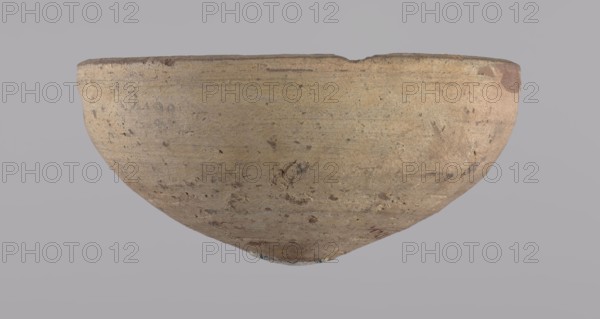 Bowl, Bowl with a conical shape and a pointed bottom. Flat, straight rim. Vessel made on the wheel of Nile clay type NB2 Vienna System classification. Surface even, irregularly covered with engobe inside and outside. Color of vessel: cream. Vessel fairly well preserved, slightly damaged in the upper part. c. 1550–c. 1069 BC, New Kingdom, Deir el-Medina. Ceramic vessel, height 6.5 cm, diameter 13.6 cm lip., A shallow, rounded bowl with a worn rim resting against a plain background, showing a textured surface with irregular spots and scuffs; the bowl appears in muted beige and tan tones with areas of light brown and small darker flecks, and the background is a soft gray.