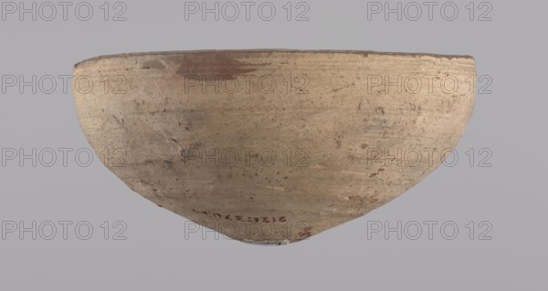 Bowl, Bowl with a conical shape and a pointed bottom. Flat, straight rim. Vessel made on the wheel of Nile clay type NB2 according to the Vienna System classification. Surface even, irregularly covered with engobe inside and outside. Color of vessel: cream. Vessel fairly well preserved, slightly damaged in the upper part. c. 1550–c. 1069 BC; New Kingdom, Deir el-Medina. Vessel; height 6.5 cm, diameter 13.6 cm lip., A large rounded bowl-like object viewed from below against a plain gray background, showing a textured surface in shades of beige, tan, light brown, and small areas of darker brown, with some rough patches and subtle surface irregularities and faint marks.