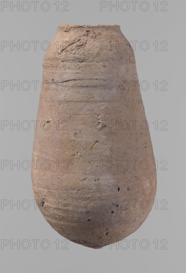 Vessel, Egyptian pottery ceramic clay vessel, New Kingdom, from Deir el-Medina, vessel, height 18.5 cm, diameter 5.2 cm rim, diameter 10.2 cm body, A roughly oval, tall ceramic vessel with a rounded base and narrow slightly flared rim, shown against a plain light gray background; the surface is textured and uneven with visible scratches, small pits, and irregularities, and the overall color palette includes muted tan, beige, light brown, and subtle grayish tones with tiny darker specks.