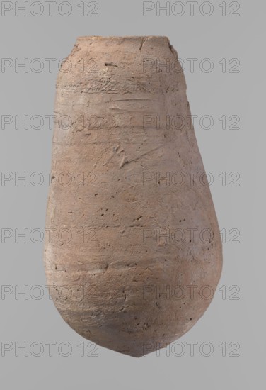 Vessel, Egyptian pottery ceramic clay vessel, New Kingdom, from Deir el-Medina; vessel, height 18.5 cm, rim diameter 5.2 cm, body diameter 10.2 cm., A roughly egg-shaped clay vessel with a narrow opening and a rounded base, showing a rough, textured surface with visible tool marks and small pits; the vessel appears in shades of light brown, tan, beige, and hints of gray against a plain gray background.