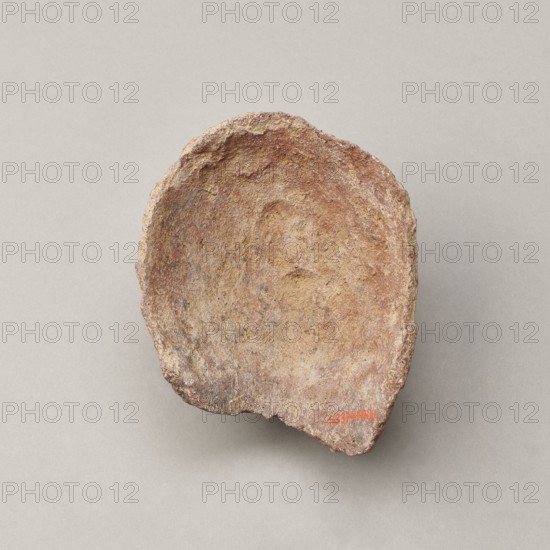 Female votive head. Female head with long, straight hair falling to the shoulders. Neck partially preserved. Elongated face with a receding forehead characterized by wide-open eyes set shallowly under prominent eyebrow arches. Mouth slightly open with fleshy lips, protruding chin, and full cheeks. 2nd century BC, Etruria; votive. Height 20 cm, width 12 cm, depth 8.5 cm, weight 0.94 kg., A roughly oval, shallow bowl-like object with a rough, irregular rim and textured surface in shades of brown, tan, reddish-brown, and gray, set against a smooth light gray background.