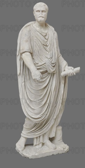 Roman statue, unknown Roman workshop. The figure of a standing man dressed in a tunic and toga, depicted in contrapposto. The right arm is exposed from the elbow, the left is almost completely hidden under the toga. Head from another statue. The face is small, with short stubble laid flat but carefully modeled. The mouth is compact, the corners turned slightly downward. The eyes are large, shadowed by drawn-down eyebrows, with a marked iris and pupil. Rectangular base, unprofiled. 1st–3rd century torso ca. mid-1st century AD; head 3rd quarter of 3rd century AD, Roman Empire 27 BC–476. Sculpture, weight 870 kg., A full-length marble statue of a bearded man wearing a long, draped robe with many folds, standing on a rectangular base; he holds a rolled object in one hand while the other arm hangs relaxed, and his feet are visible beneath the drapery with one foot slightly forward; the sculpture is carved in white stone with subtle variations in tone and weathering, set against a plain gray...