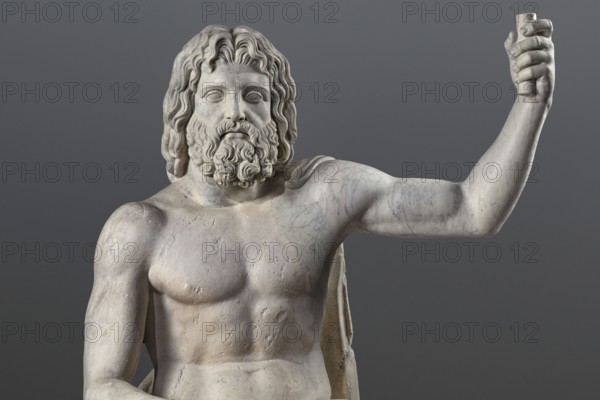 Statue of Jupiter of the Capitoline type, unknown Roman workshop. Jupiter Zeus seated on a throne set on a rectangular base. Zeus sits stiffly with his torso slightly back. His raised left hand holds a scepter; his right hand rests casually on his right knee. The right foot is slightly forward. The legs are covered with a himation, which also covers the back and left shoulder. The muscular torso, strongly developed at the shoulders, has naturalistic modeling. The head is disproportionately large, and the face is perfect with a slightly open mouth. The hair is parted from the center anastole. The beard is thick, arranged in strands on the sides and in curls on the chin. Roman sculpture, Roman copy after a Hellenistic variant of Phidias's statue of Zeus the Olympian. Late 2nd–3rd century AD. Sculpture, weight 930 kg., A large pale stone statue of a bearded male figure is shown from the waist up against a smooth gray background; the statue has wavy hair and a detailed curly beard, a bare ...