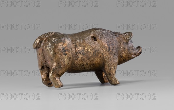 A small bronze figurine of a pig. The animal stands on rather schematically depicted legs ending in forward-pointing hooves. The animal's massive body is characterized by an unnatural length. The torso is adorned with a small, doubled tail. The presence of hair is clearly marked on the animal's back. The pig's muzzle, set on a thick neck, ends in a narrow snout. The pig's slightly protruding ears point forward. The animal's eyes, which are unusually large relative to the rest of the body, are clearly marked. The sculpture is covered with a natural patina. The figurine was probably used as a votive offering; this interpretation is supported by its finding in the vicinity of the temple. Hellenistic period, Kyrene Libya. Figurine. Height 1.8 cm; width 4.2 cm; depth 1.4 cm; weight 0.035 kg., A small sculpted figure of an animal resembling a pig is shown in profile on a smooth surface, with a rounded body, short legs, a curled tail, and a snout; the surface of the figure is textured with ir...