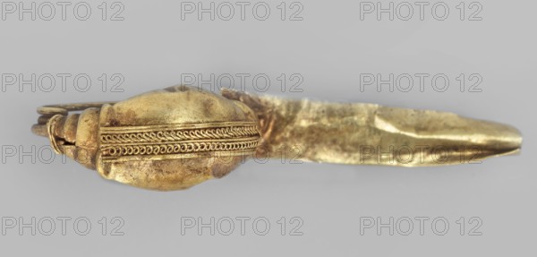 Leech fibula with an elongated stem. Brooch, goldsmithery; leech fibula with a long sheath. The swollen, profiled ring at the ends is decorated with a long strip of filigree in the form of figure eights. The spring has 1 1/2 coils. 2nd half of the 6th century BC, Etruria. Jewelry, fibula. Height 1.2 cm, width 3 cm, depth 0.6 cm, weight 1 g., A close-up view of a metal object with a rounded, elongated central portion and a flattened protruding section, shown against a neutral background. The central portion has decorative raised bands with repeating looped patterns running along its length and a slightly irregular, worn surface texture. The protruding section appears flat and tapered with uneven surfaces and dents. A curved looped element is visible at one end, connecting parts of the object. Visible colors include gold, brass, and areas of darker brownish tarnish, with the background appearing light gray.