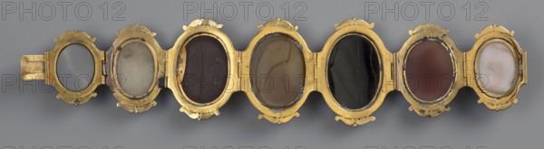 Bracelet with cameos, made by, Roniker, E. - purchased, ancient Roman-period/19th century AD goldsmithery jewelry, portraits, gems, cameos, height 4.2 cm, width 19.5 cm, A horizontal row of linked oval frames made of a metallic gold material holds a series of rounded insets in varying muted colors; from left to right there is an empty oval with a gray background, a pale off-white inset with faint darker smudges, a deep brown inset, a warm tan inset with subtle streaks, a glossy black inset with a vertical seam, a reddish-brown inset, and a creamy white inset with light tan veins; the gold frames show small decorative tabs and slight wear, and the overall background is a neutral gray.