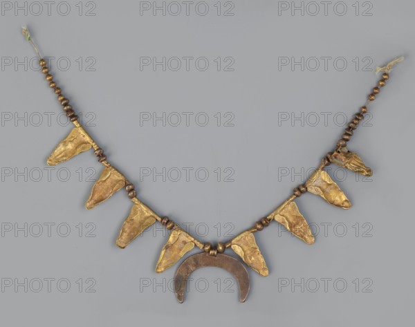 Necklace with eight amphorae and a crescent, Necklace of gold with crescents ornament, goldsmithing. The necklace consists of eight gold amphorae; the surface between the bodies and the necks of the amphorae is filled with white enamel. Each amphora is attached to a fluted tube. Two gold beads are placed between the amphorae. At the ends of the necklace are 10 beads on one side and 11 beads on the other. In the center hangs a flat crescent moon, facing downwards, made of a more reddish gold. Dated to the 3rd century BC possibly late 4th–3rd century BC, probably Greece. Jewelry; weight 12 g., A necklace displayed against a light gray background, composed of a strand with a group of small round beads along each side in brown tones, interspersed with a series of irregular triangular pendants in a metallic gold color, and a central crescent-shaped pendant in a darker bronze-brown hue; the gold triangular pieces hang downward and show uneven, textured surfaces, while the beads are smooth an...