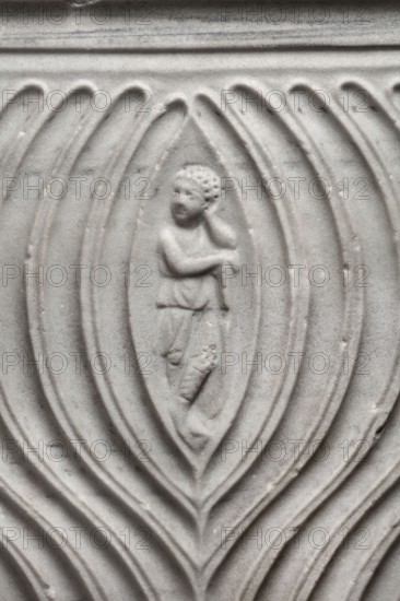 Sarcophagus with a depiction of a married couple and a shepherd, unknown Roman workshop. A large Roman sarcophagus with strigilla S-shaped grooves on the front forming a central medallion, decorated with a standing, thoughtful shepherd leaning on a staff pedum. Flanking the central medallion are figures presumed to be the deceased, standing against draped fabrics parapetasmata: on the left, a woman in a tunic and long cloak palla holding a scroll volumen in her left hand; on the right, a man in a tunic and toga with contabulatio a specially wrapped hem, holding a scroll in his left hand and wearing mullei leather military boots. Both frontal figures have incompletely finished heads. The side walls show reliefs of a seated griffin with a lion's head; the left wall near its lower left corner contains an opening to the interior, and the lower left corner of the right wall is missing. The rear wall is rather carelessly worked. Numerous abrasions and damage, particularly to the corners and ...