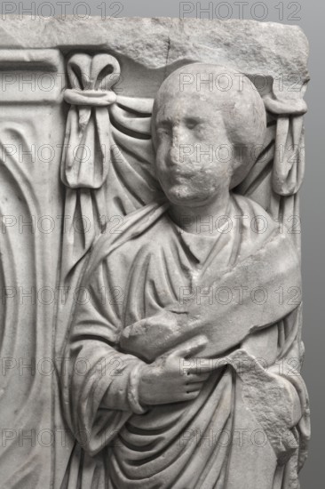 Sarcophagus with a depiction of a married couple and a shepherd, unknown Roman workshop. A large Roman sarcophagus with strigilla S-shaped grooves forming a central medallion, decorated with a standing, thoughtful shepherd leaning on a staff pedum. On the front sides are figures of the presumed deceased standing against draped fabrics parapetasmata: left, a woman in a tunic and long cloak palla holding a scroll volumen in her left hand; right, a man in a tunic and toga with a contabulatio specially wrapped hem holding a scroll in his left hand and wearing mullei leather military boots. Both frontal figures have incompletely finished heads. The side walls show reliefs of a seated griffin with a lion's head; the left side near its lower left corner has an opening to the interior, and the lower left corner of the right wall is missing. The rear wall is more roughly worked. Considerable abrasions and damage, particularly to the corners and the figures on both sides of the front wall. Circa...