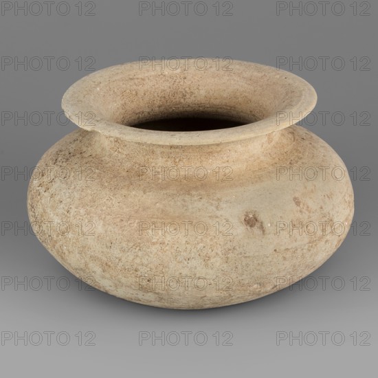 Vessel, unknown northern Mesopotamian workshop; viseless vessel for oils and ointments; low vessel with an ellipsoidal belly with a rounded bottom, low neck, and wide, upturned rim. 1st half of the 3rd millennium BC; Early Jazira III period, Northern Mesopotamia Khabur Basin, Tell Rad Shakra Northeastern Syria. Vessel; height 6.8 cm, width 10.8 cm, weight 200 g., A rounded earthenware vessel with a wide flared rim and a short neck, displaying a weathered, textured surface in beige and light tan tones with patches of darker brown and pale off-white speckles, set against a smooth neutral gray background.