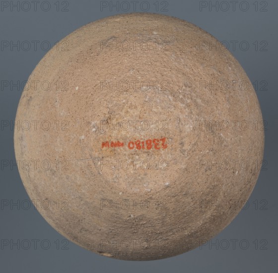 Bowl, unknown Northern Mesopotamian workshop, Early Jazira III period ca. 2600–ca. 2350 BC; Early Dynastic III period, clay. Bowl with a flat, obliquely cut round bottom, gently sloping walls that straighten in the upper part and bend slightly inward, ending in a straight, non-distinctive rim. Before firing a potter's mark was incised at the bottom: two intersecting lines of varying lengths, the shorter running parallel to the bottom and the longer starting at the belly and reaching half the bottom diameter. Northern Mesopotamia Khabur basin, Tell Rad Shakra, northeastern Syria., A roughly spherical, textured object with a coarse, grainy surface in shades of light tan, beige, and sandy brown sits against a solid gray-blue background; the sphere shows areas of slightly darker brown discoloration and small white speckles, with a shallow, uneven depression near its visible center.