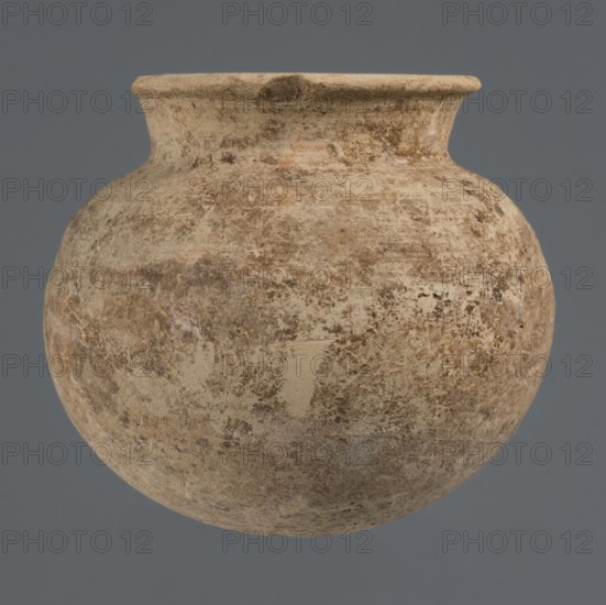 Globular vessel, unknown Northern Mesopotamian workshop, clay, Early Jazira III period ca. 2600–ca. 2350 BC; Early Dynastic III period, globular vessel with a low, conically flaring neck terminating in a narrow, slightly thickened and everted rim; rounded, slightly flattened bottom; ca. 2600–ca. 2350 BC; Syria, Northern Mesopotamia Khabur basin, Tell Rad Shakra north-eastern Syria; height 8.4 cm, width 9.5 cm, A rounded ceramic vessel with a narrow neck and flared rim suspended against a neutral background, showing a weathered, mottled surface in shades of beige, tan, brown, and hints of gray with areas of lighter and darker spotting and textured patches.