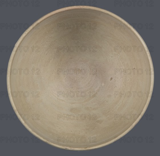 Bowl, unknown Northern Mesopotamian workshop; clay; Early Jazira III period ca. 2600–ca. 2350 BC / Early Dynastic III period; tableware vessel. Bowl with a flat, slightly oblique, oval bottom with traces of being cut off with a string, gently tilted walls that straighten and bend slightly inwards in the upper part, and a straight, undifferentiated rim. Northern Mesopotamia Khabur basin, Tell Rad Shakra Northeastern Syria., A top-down view of a round, shallow bowl with a smooth interior surface showing subtle circular marks and variations in texture, in beige and light tan tones with small darker speckles; the bowl sits against a flat, dark gray background.