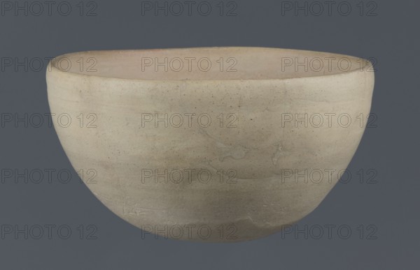 Bowl, unknown Northern Mesopotamian workshop, clay, Early Jazira III period ca. 2600–ca. 2350 BC / Early Dynastic III period. Tableware bowl with a flat, slightly oblique oval bottom with traces of being cut off with a string; gently tilted walls that straighten and bend slightly inwards in the upper part; straight, undifferentiated rim. Northern Mesopotamia Khabur basin, Tell Rad Shakra., A simple rounded bowl shown against a solid background, with a smooth matte surface and subtle irregularities; the bowl appears mostly in beige and light tan tones with faint variations and speckling, and the interior shows slightly warmer pale beige and pinkish-beige hues, while the background is a muted gray-blue.
