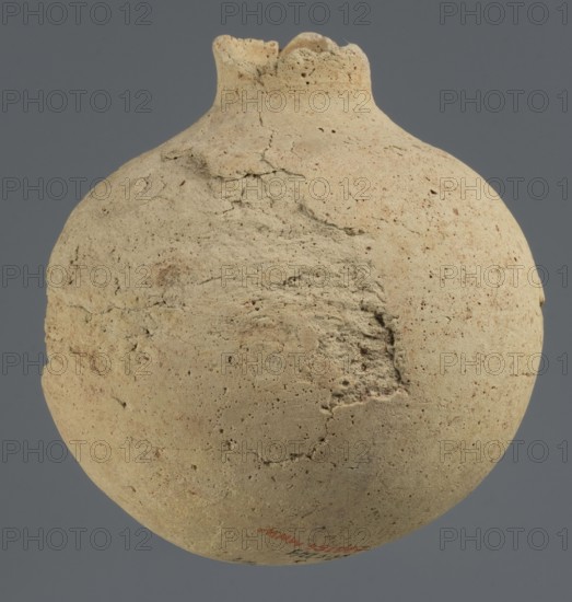 Globular vessel, unknown Northern Mesopotamian workshop, Early Jazira III period ca. 2600–ca. 2350 BC / Early Dynastic III period; globular vessel with a narrow neck upper part of neck and spout not preserved, thickened circular base; clay; function: vessel for oils and ointments; vice-free vessel; origin: Northern Mesopotamia Al-Jazira, Khabur basin, Tell Rad Shakra, Syria; height 11.3 cm, width 10.45 cm., A rounded, weathered vessel with a narrow, irregular rim sits against a flat gray background; the vessel surface is rough and pitted with a sandy beige color and subtle variations of light tan and pale brown, with a few darker brown speckles and scattered areas of slightly darker, earthy beige where the texture is more eroded.