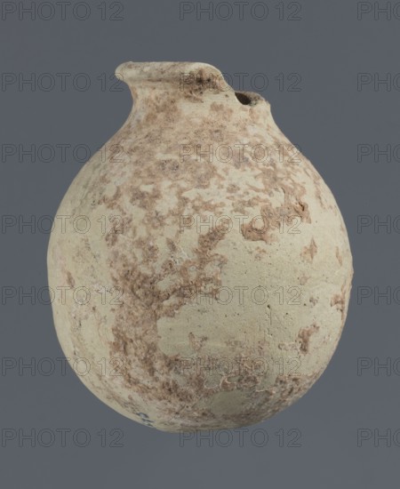 Spherical vessel, unknown northern Mesopotamian workshop, clay, Early Jazira III period ca. 2600–ca. 2350 BC; Early Dynastic III period, Al-Jazira northern Mesopotamia, Khabur basin, Tell Rad Shakra Tell Rad Shakrah?, North-Eastern Syria; spherical vessel with an egg-shaped belly, rounded bottom, low cylindrical neck with thickened outward-turned rim; height 7.8 cm, width 6.5 cm., A rounded ceramic jug with a short neck and a slightly flared rim, shown against a flat gray background; the jug surface is mottled with pale beige and off-white base tones and irregular patches of light to medium brown encrustation, with a rough, weathered texture and small pits and flaking across its body.