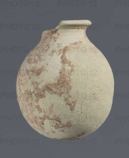 Spherical vessel, unknown northern Mesopotamian workshop, clay, Early Jazira III period ca. 2600–ca. 2350 BC / Early Dynastic III period, Northern Mesopotamia Khabur basin. Spherical vessel with an egg-shaped belly with a rounded bottom and a low cylindrical neck ending with a thickened rim turned outwards. Found at Tell Rad Shakra, North-Eastern Syria. Height 7.8 cm; width 6.5 cm., A rounded ceramic vessel with a narrow neck and flared rim sits against a solid gray background; the vessel surface is mostly pale beige to off-white with areas of mottled brown and tan discoloration and visible fine cracks and rough texture across its body, and the rim shows a slightly darker, weathered edge.
