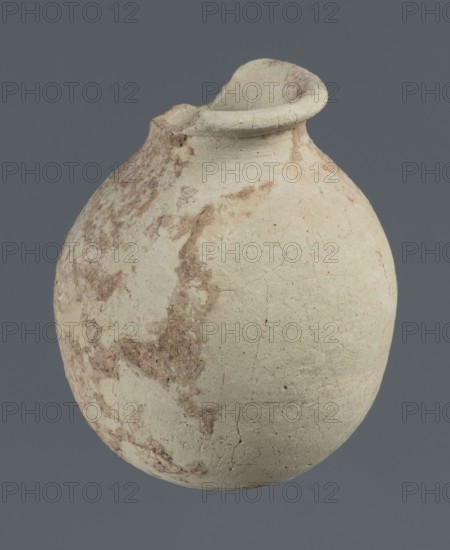 Spherical vessel, unknown northern Mesopotamian workshop; clay; Early Jazira III period / Early Dynastic III period ca. 2600–ca. 2350 BC. Spherical vessel with an egg-shaped belly, rounded bottom, low cylindrical neck ending in a thickened rim turned outwards. Origin: Northern Mesopotamia Khabur basin, Tell Rad Shakra, Syria. Vessel; height 7.8 cm, width 6.5 cm., A rounded clay vessel with an uneven rim and a small poured spout, showing a weathered surface with patches of brown discoloration and fine surface cracks, set against a solid gray background; visible colors include off-white, beige, brown, and gray.