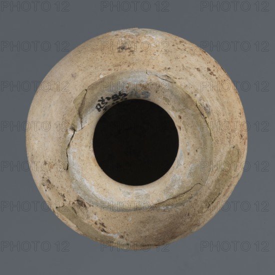 Vessel with an ellipsoidal belly, unknown northern Mesopotamian workshop, Early Jazira III period ca. 2600–ca. 2350 BC / Early Dynastic III period ca. 2600–ca. 2350 BC; clay vessel for oils and ointments; a small vessel with an ellipsoidal belly, rounded bottom, low flared neck ending in a flat top thickened by an outward curl; Al-Jazira Khabur basin, Northern Mesopotamia Tell Rad Shakra, northeastern Syria; height 7.4 cm, width 8.6 cm., A round, top-down view of a weathered pottery vessel with a dark central opening, the rim and body showing a mottled surface of beige, tan, and light brown with patches of pale gray and hints of olive-green discoloration, some hairline cracks and flaking on the rim and shoulder, and a smooth gray background surrounding the object.
