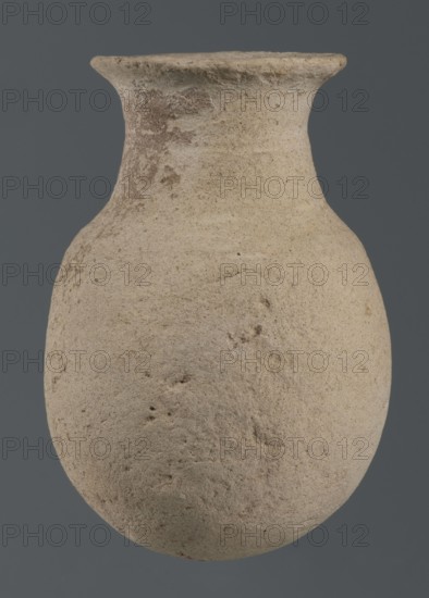 Flask, unknown northern Mesopotamian workshop, Early Jazira IV period ca. 2350–ca. 2200 BC / Akkadian period ca. 2350–ca. 2200 BC. Flask-shaped vessel with an egg-shaped belly, a rounded bottom, a high cylindrical neck separated from the belly by narrow shoulders and ending with a flat, tilted rim. Syria, Northern Mesopotamia Khabur basin, Tell Rad Shakra. Vessel; height 14.5 cm, width 9 cm., A weathered rounded vessel with a narrow neck and flared rim, shown against a plain dark gray background; the vessel surface is rough and granular with irregular pits and patches, displaying mainly beige and light tan tones with areas of light brown and subtle grayish speckling.
