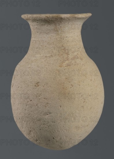 Flask, unknown northern Mesopotamian workshop, vice-free vessel, tableware, excavations of the Centre of Mediterranean Archaeology, Early Jazira IV period ca. 2350–ca. 2200 BC, Akkadian period ca. 2350–ca. 2200 BC. Flask-shaped vessel with an egg-shaped belly, a rounded bottom, a high cylindrical neck separated from the belly by narrow shoulders and ending with a flat, tilted rim. ca. 2350–ca. 2200 BC; Syria, Northern Mesopotamia Khabur basin, Tell Rad Shakra Northeastern Syria. Vessel, height 14.5 cm, width 9 cm., A single rounded clay vessel fills the frame, showing a bulbous body that tapers into a narrower neck with a flared rim; the surface appears rough and slightly pitted with irregular texture and small depressions. The vessel displays a range of earthy colors including beige, light tan, sandy brown, and hints of pale ochre, with subtle darker speckles and faint mottled patches. The background is a uniform dark gray, and the lighting reveals soft shadows and gentle highlights t...
