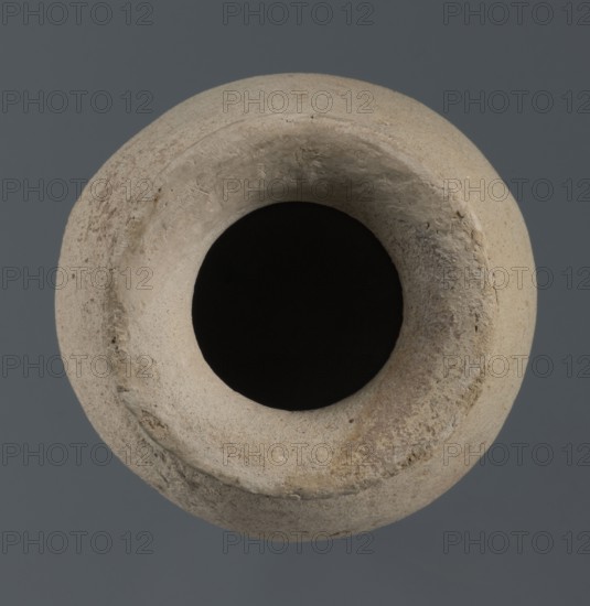 Flask, unknown northern Mesopotamian workshop; Early Jazira IV period ca. 2350–ca. 2200 BC / Akkadian period ca. 2350–ca. 2200 BC. Flask-shaped vessel with an egg-shaped belly, a rounded bottom, a high cylindrical neck separated from the belly by narrow shoulders, and ending with a flat, tilted rim. Syria, Tell Rad Shakra Khabur basin, Northeastern Syria; Northern Mesopotamia place of production. Vessel; height 14.5 cm, width 9 cm., A top-down view of a round pottery vessel with a wide circular opening and thick rim, showing a rough textured surface and irregular wear. The vessel appears in shades of beige, tan, off-white, and light brown with darker brown patches and flecks, and the interior opening is deep black. The background is a flat dark gray.