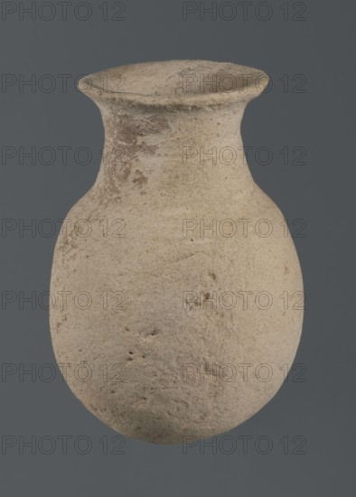 Flask, unknown northern Mesopotamian workshop; vice-free vessels, tableware; excavations of the Centre of Mediterranean Archaeology, University of Warsaw; Early Jazira IV period ca. 2350–ca. 2200 BC, Akkadian period ca. 2350–ca. 2200 BC; flask-shaped vessel with an egg-shaped belly, a rounded bottom, a high cylindrical neck separated from the belly by narrow shoulders and ending with a flat, tilted rim; ca. 2350–ca. 2200 BC; Syria, Northern Mesopotamia Khabur basin; Tell Rad Shakra Northeastern Syria; vessel; height 14.5 cm, width 9 cm, A roughly oval, bulbous ceramic vessel with a flared rim and narrow neck, shown against a solid gray background; the surface of the vessel is textured and weathered with an overall beige color and patches of light brown and darker brown discoloration, along with small pits and rough areas visible across its body.