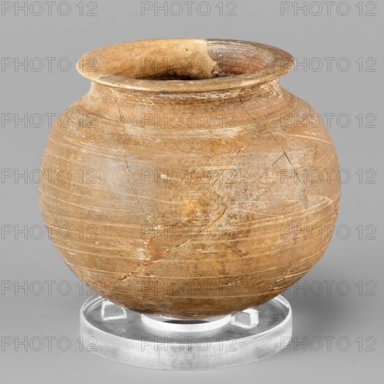 Vessel, unknown Northern Mesopotamian workshop, vice-free vessel for oils and ointments, spherical vessel. Low vessel with a spherical belly, rounded bottom and low, wide neck with a narrow, upturned spout. The vessel was smoothed and fired in a reduction atmosphere. 1st half of the 3rd millennium BC; Early Jazira III period, Northern Mesopotamia Khabur basin, Tell Rad Shakra North-eastern Syria. Material culture; excavations of the Centre of Mediterranean Archaeology, University of Warsaw. Vessel; height 6.1 cm, width 6.9 cm, weight 85 g., A rounded ceramic pot with a flared rim sits on a clear circular stand, showing a surface of warm brown and tan tones with lighter beige streaks and areas of darker brown near the mouth; the pot displays visible hairline cracks and repair lines, faint horizontal tool marks encircling its body, subtle surface abrasions, and a few small chips along the rim, while the stand appears translucent white against a neutral light gray background.